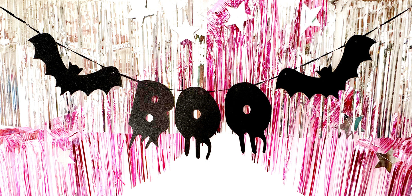 Halloween-themed decorative banner with black bats and 'BOO' letters on a pink and white striped background.