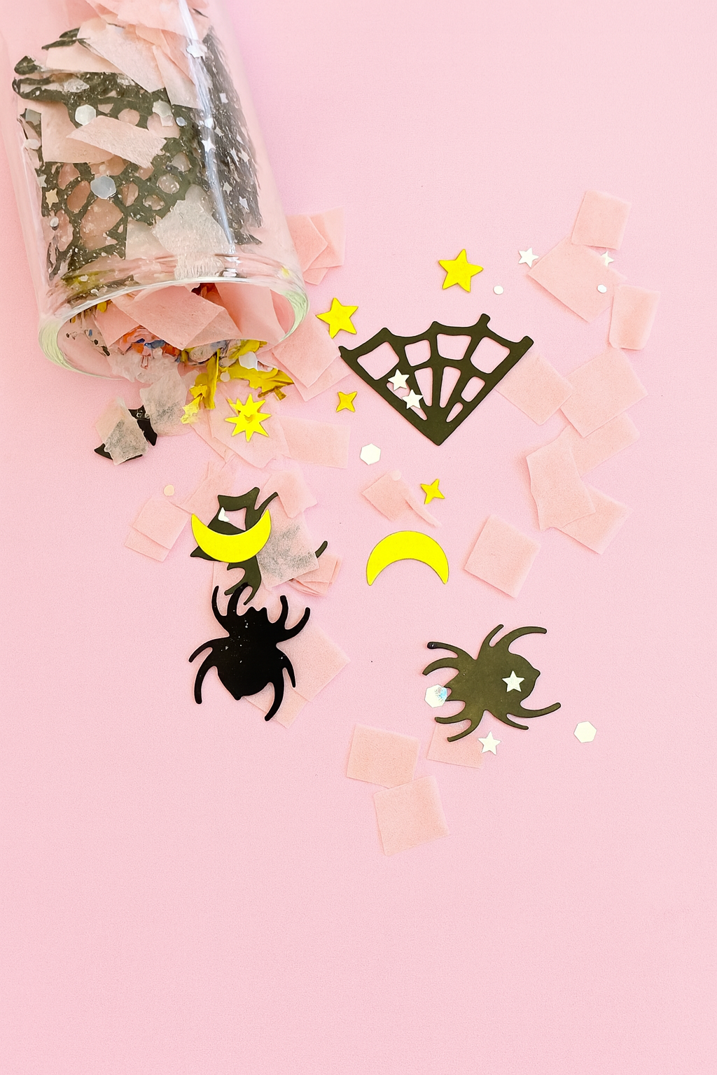 Decorative confetti with spider, moon, and web designs on a pink background