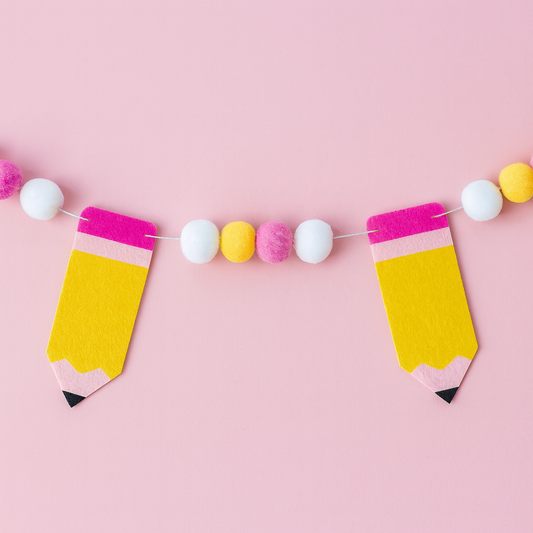 Decorative garland with pencil-shaped flags and pom-poms on a pink background