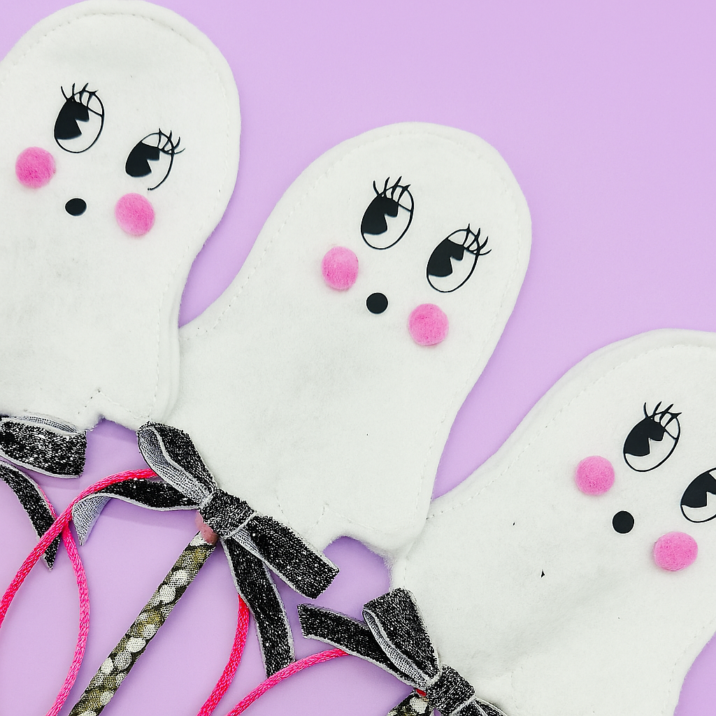 Three halloween ghost wands with bow ties on a purple background