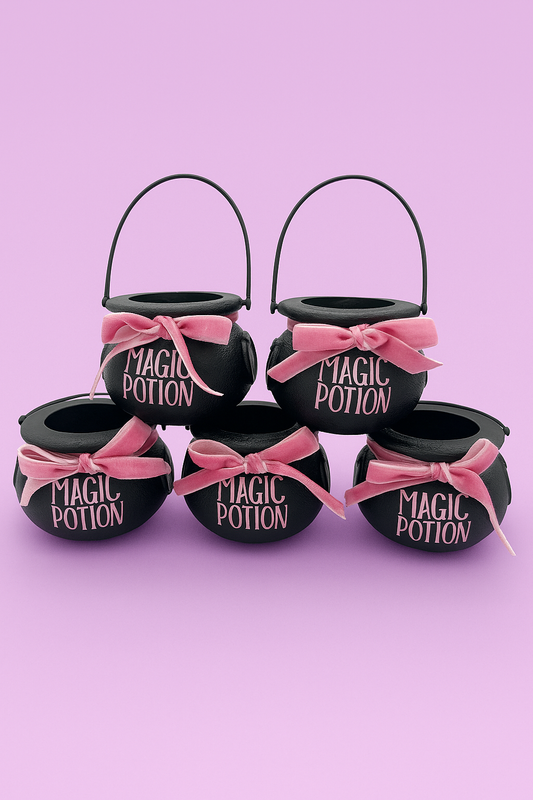 Black Halloween cauldrons labeled 'Magic Potion' with pink bows on a pink background