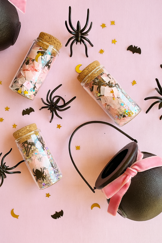 Halloween-themed items including jars with decorative confetti and a headband on a pink background.