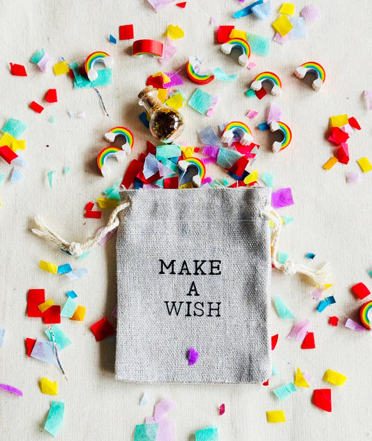 Small bag labeled 'MAKE A WISH' surrounded by colorful confetti and rainbow decorations on a light background.