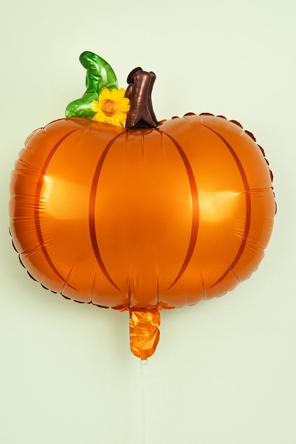 Pumpkin-shaped balloon with a green stem and yellow flower on a light green background