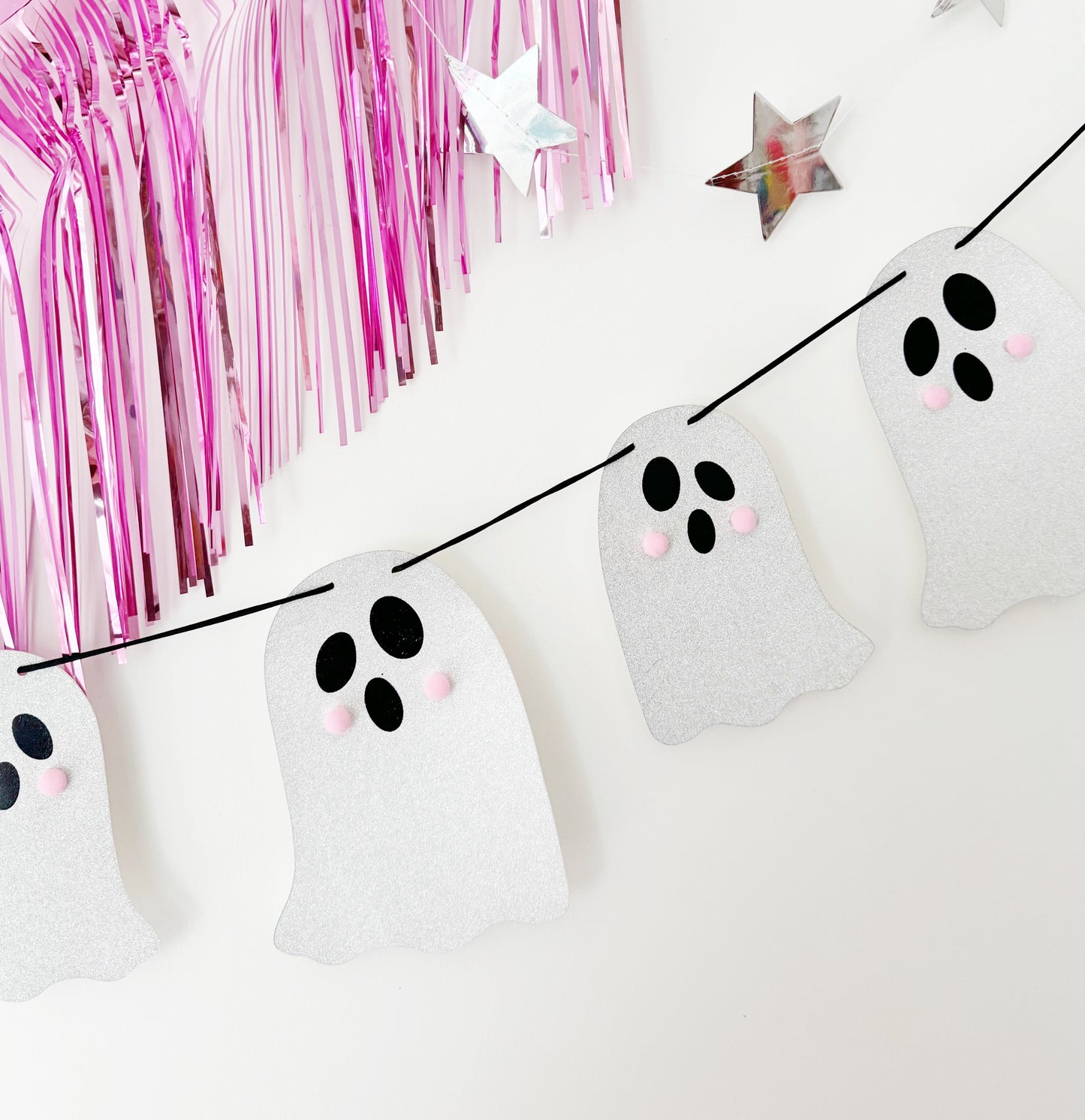 Halloween-themed ghost decorations on a string with pink tinsel in the background.