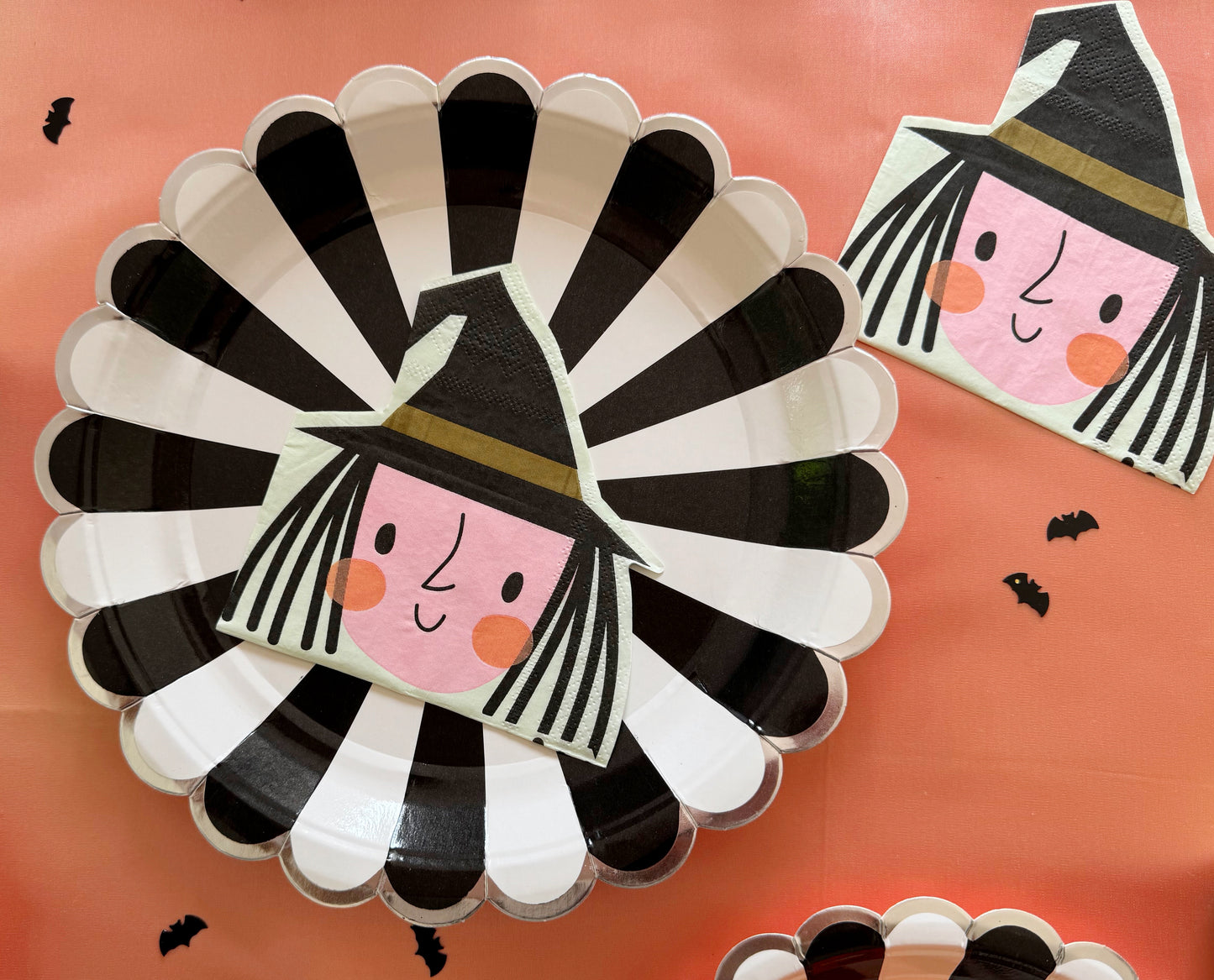 Halloween-themed paper plates with witch napkins on a pink background