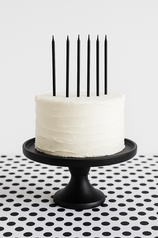 White cake with black candles on a black cake stand against a white background