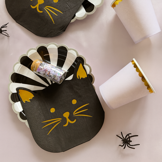 Halloween-themed paper plates and cups with black cat designs on a light pink background.