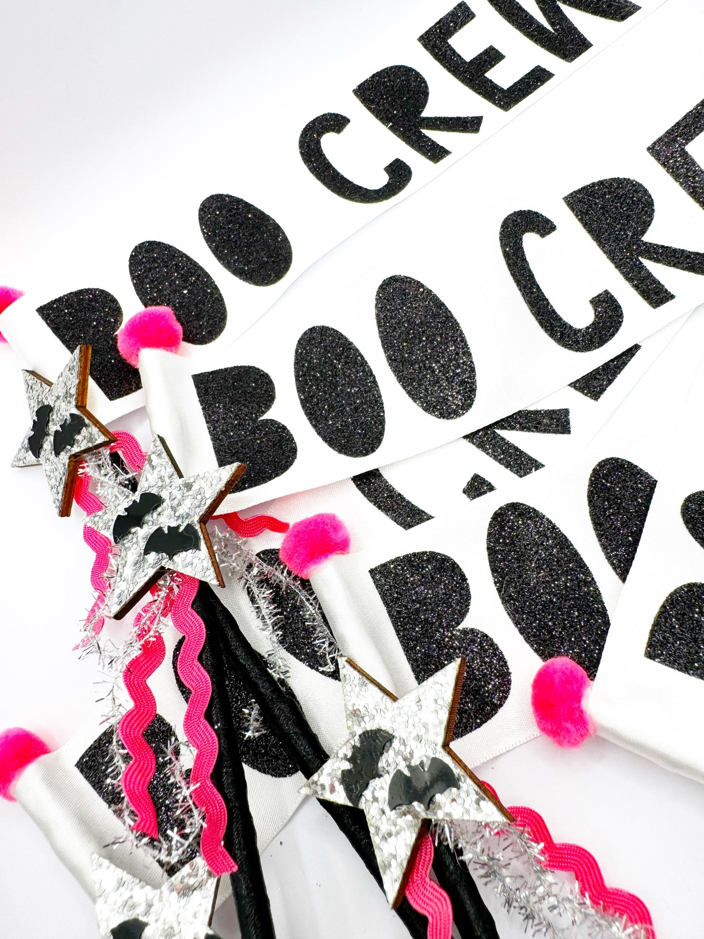 Decorative halloween boo crew wands with black glittery text, pink pom-poms, and decorative ribbons on a white background.