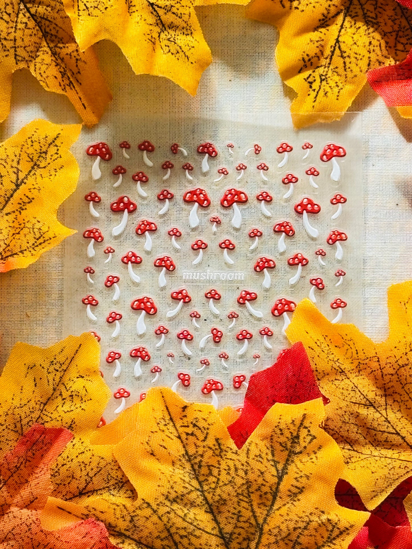 A sheet of mini toadstool nail stickers textured surface with yellow leaves around.