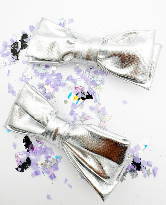 Two silver bow hair clips on a white background with colourful confetti.