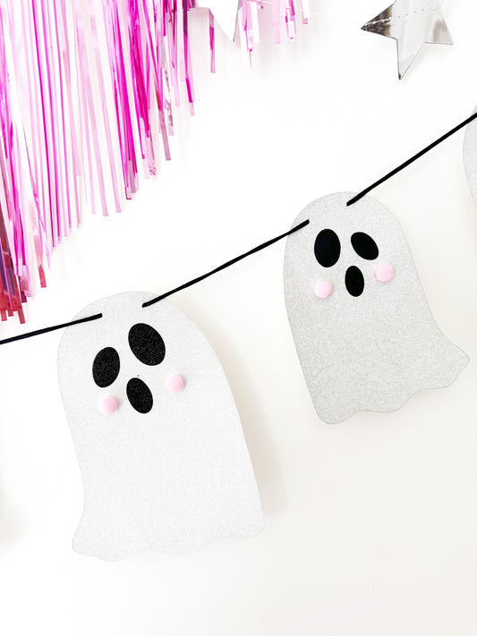 Halloween-themed ghost decorations on a string with pink tinsel in the background.